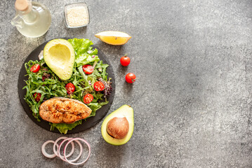 grilled salmon steak and fresh green vegetable tomato salad with lettuce and avocado on stone background with copy space for your text