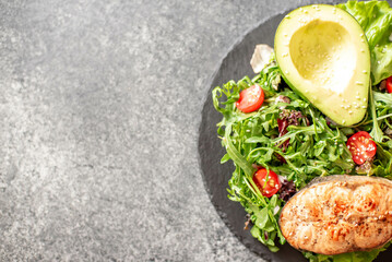 grilled salmon steak and fresh green vegetable tomato salad with lettuce and avocado on stone background with copy space for your text