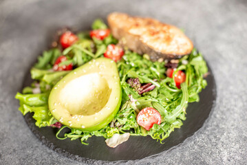 grilled salmon steak and fresh green vegetable tomato salad with lettuce and avocado on stone background