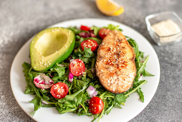 grilled salmon steak and fresh green vegetable tomato salad with lettuce and avocado on stone background
