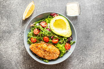 grilled salmon steak and fresh green vegetable tomato salad with lettuce and avocado on stone background
