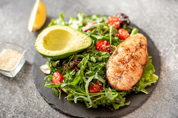 grilled salmon steak and fresh green vegetable tomato salad with lettuce and avocado on stone background