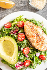 grilled salmon steak and fresh green vegetable tomato salad with lettuce and avocado on stone background