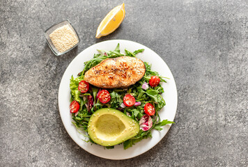 grilled salmon steak and fresh green vegetable tomato salad with lettuce and avocado on stone background