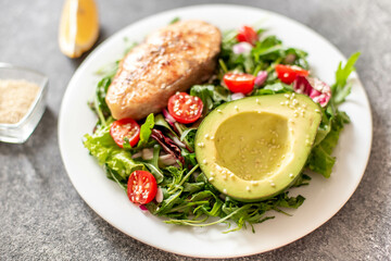 grilled salmon steak and fresh green vegetable tomato salad with lettuce and avocado on stone background