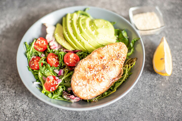 grilled salmon steak and fresh green vegetable tomato salad with lettuce and avocado on stone background