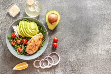 grilled salmon steak and fresh green vegetable tomato salad with lettuce and avocado on stone background with copy space for your text