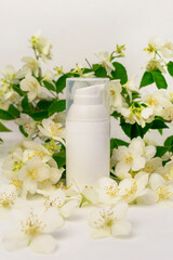 Fototapeta na wymiar A white cosmetic jar with a dispenser against the background of fragrant white flowers and green leaves of an ornamental shrub. Jasmine or Philadelphus. Body or face cream mockup.