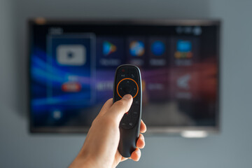 Close-up of male hand using remote of modern smart tv on background of television.
