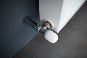 Close-up of valve of heating radiator of white on a grey wall.