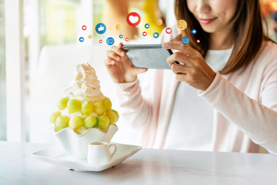 Young woman taking photo of bingsu with smart phone in restaurant and uploading the photos to the social media in cafe, Modern lifestyle concept
