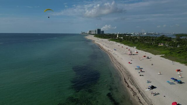 Aerial view of a beautiful sunny day at the beach when a powered paraglider or powered parachute comes into view.