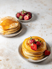 Two plates of homemade pancakes with strawberry and honey on textured background in rustic style