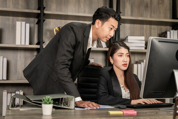 An Asian business executive inspects the work of a female employee at her laptop. Talk with smiling faces and have fun and relax. at the office of the company