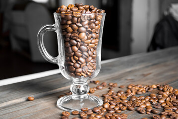 Coffee beans on a wooden bar counter. On the wooden table is a glass cup with coffee beans.