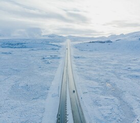 Beautiful aerial shot of a wet highway in the middle of snow-capped field on a winter day in Iceland