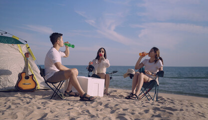 Group of happy Asian young friends sitting on camping chairs holding and drinking colored soft...