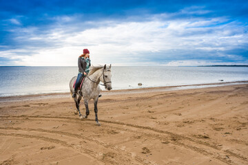 dressing jeans, jacket and fall hat female rider is in the saddle along shore