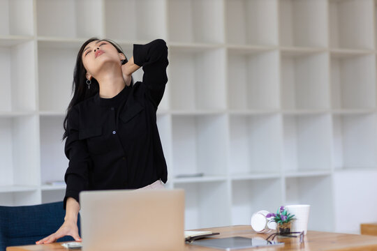 Young female worker in an office stretches to relieve aches and pains from work.