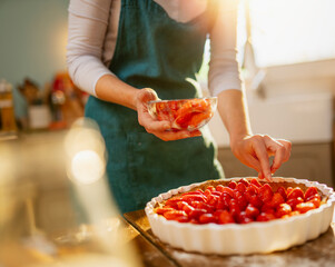 Young woman making a strawberry pie, in the kitchen. the sun enters through the window
