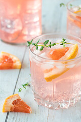 Close up of a grapefruit spritzer beverage garnished with grapefruit and thyme.