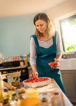 Young woman making a strawberry pie, in the kitchen. the sun enters through the window
