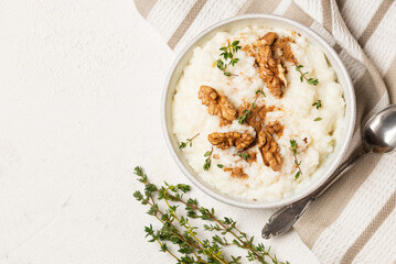 Top view of creamy rice pudding topping whith walnuts and thyme in white plate with teaspoon on...