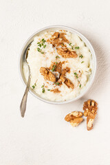 Isolated creamy rice pudding sprinkled in the cinnamon powder and top with walnuts and thyme in a white plate with teaspoon on white textured background