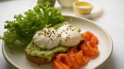 Chef sprinkles seeds on toast with poached eggs and guacamole. Delicious toast served with trout slices and fresh salad leaves extreme closeup