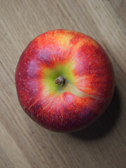 One big red apple on a wooden table, a close-up shot. Top view.
