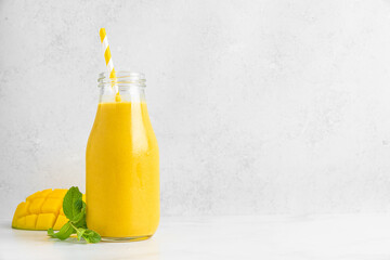 Mango smoothie or milkshake in a glass bottle with straw, fresh fruit and mint on white background