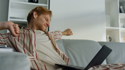 Fototapeta premium Tired guy browsing web at home office closeup. Sleepy manager stretching body