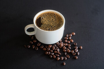 Cup full of coffee with bubbles and black coffee beans on black background.