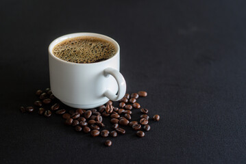 Cup full of coffee with bubbles and black coffee beans on black background.