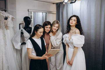 Fototapeta premium Bride at the clothes shop for wedding dresses she is choosing a dress and the designer is assisting her
