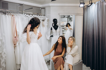 Obraz premium Beautiful bride is trying on an elegant wedding dress in modern wedding salon, her friends are helping