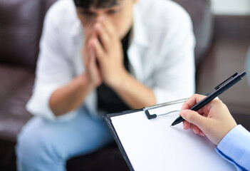 A stressed man consults a psychiatrist on family issues, love, work, and money, A psychiatrist is calming an Asian man suffering from depression in a medical clinic or hospital exam room office.