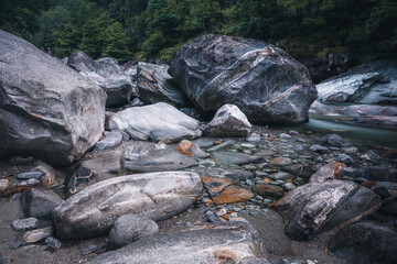 Atmosphärischer Naturhintergrund mit riesigen Steinen im Bergfluss. Große Felsen im mächtigen Wasserstrom, Nahaufnahme. Naturhintergrund mit Wald. Dunkel türkisblauer Fluss mit Steinen.