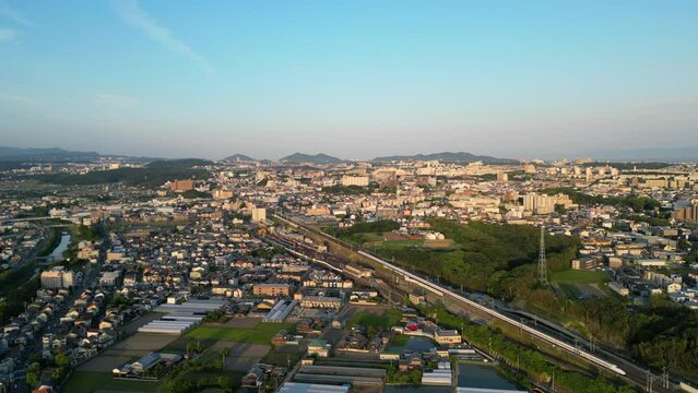Aerial view of Shinkansen rolling through sprawling Japanese suburbs in late afternoon