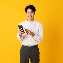 Young good looking asian man using smartphone isolated on yellow background pointing on screen