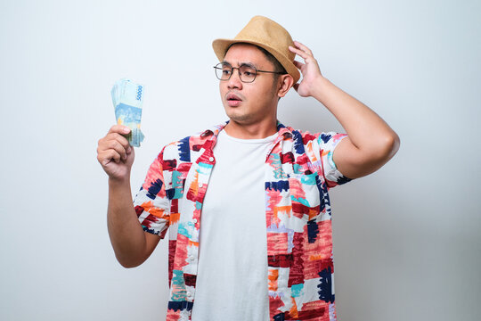 Young Asian man holding paper money and showing confused face expression