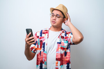 Young asian man holding a phone looking sideways with doubtful and skeptical expression.