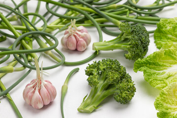 Broccoli, cabbage leaves, garlic and green garlic pods on white
