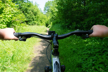 Fototapeta na wymiar Biking in the city park. View through the eyes of bikers. Hands on the handlebars of a bicycle close-up