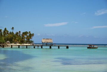 View of the turquoise sea with a dock and a boat on the water surface against the blue sky.