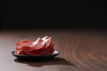 saucer with this slices of bresaola on walnut wood table