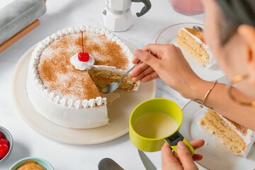 Woman pours cream on the sponge cake decorated with maraschino cherry