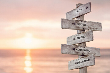 faith prayer fasting almsgiving pilgrimage text engraved on wooden signpost by the ocean during sunset. five pillars of islam.