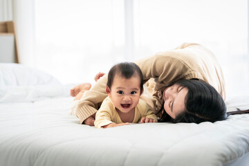 Obraz na płótnie Canvas baby girl with asian mom smiling baby happily playing together in bed in the bedroom at home