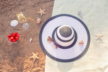 Hat, sunglasses, champagne, strawberry, starfishes and seashells on towel on sand beach.